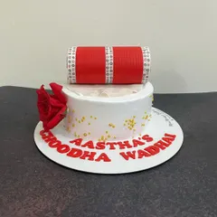 A special cake for a 'Choodha Wadhai' ceremony. This design features a handcrafted, edible 'choodha' on top of a clean white cake, accented with a fondant rose and the bride's name.