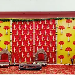 A bold and vibrant stage setup for a pre-wedding event. The decor uses a striking combination of red and yellow with lotus motifs, creating a festive and eye-catching backdrop.