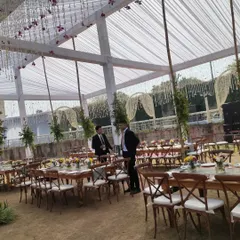 A view of the guest seating arrangement during the setup of an outdoor event. This image shows the scale of the tent and the layout of long wooden tables and chairs, ready for place settings.