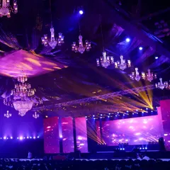 The calm before the storm of celebration. This wide shot shows the scale of a concert-style reception, with dozens of chandeliers suspended over the hall and a massive stage, all lit in dramatic purple and gold hues.
