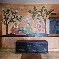 A scene of daily life unfolds on this wall, showing women preparing for the day outside their home, complete with the apartment number integrated into the traditional design.