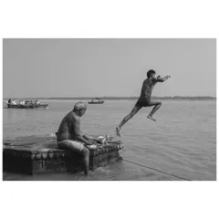 A dynamic black and white shot of a boy leaping into the Ganga at Varanasi. The image freezes the motion, capturing a moment of youthful exuberance against the backdrop of river life.