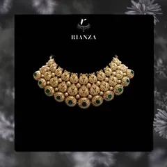 A grand gold necklace featuring intricate nakshi work and studded with green stones. This type of design is inspired by South Indian temple jewellery and is perfect for a traditional ceremony.