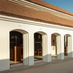 The facade of the hotel features a series of arches, creating a rhythmic transition between the exterior and interior spaces while providing shade and depth.