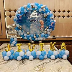 A magical Frozen-themed 5th birthday party. This grand setup includes a circular balloon frame in icy blue and silver, a custom backdrop featuring Elsa, and the birthday girl's name spelled out in foil balloons.