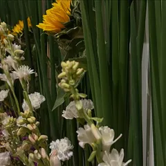 A close-up view of the fresh floral decor, showing the beautiful texture and combination of sunflowers, white carnations, and purple statice against a backdrop of green leaves.
