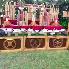 A rustic, woodland-themed buffet counter setup for an outdoor event, featuring wooden wheels and mushroom-shaped decor.