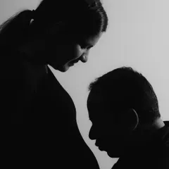 This artistic silhouette focuses on the profound connection between the father-to-be and his unborn child. The dramatic lighting strips away all distractions, leaving only the pure, emotional bond in this powerful black and white maternity photograph.