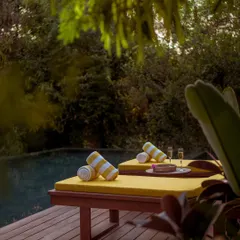 Two sun loungers are set up on the deck with champagne, ready for a relaxing afternoon. The view looks out over the pool into the dense, green forest.
