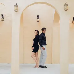 A playful, back-to-back pose in a minimalist studio setting. This shot shows the couple's fun side while maintaining a chic, fashionable aesthetic with their coordinated modern outfits.