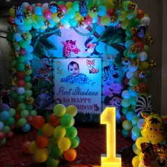 A closer look at a jungle-themed first birthday party. The setup includes a custom backdrop with the baby's name, a full balloon arch with animal prints, and a light-up number '1'.