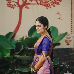A serene bridal portrait against a backdrop of traditional wall art. The bride's calm demeanor and the beautiful contrast of her purple and pink saree create a stunning image.