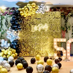 A glamorous 50th birthday party with a gold shimmer wall and a "Let's Party" neon sign. The black, gold, and silver balloons complete the luxurious theme.