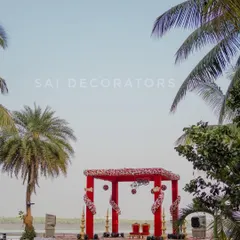 Another view of the beautiful waterside wedding mandap, framed by palm trees. The traditional red structure is decorated with floral arrangements and hanging ornaments, perfect for pheras with a view.