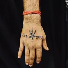 Hand tattoos make a bold statement, and we ensure they are clean and powerful. This piece features the Sanskrit shloka 'Ant asti prarambh' (the end is the beginning) combined with a Trishul, creating a striking symbol of life's cyclical nature right on the hand.
