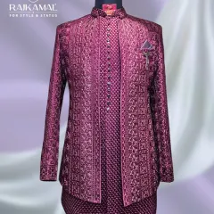A full view of a magnificent magenta Jodhpuri suit. The all-over embroidery and long shirt style create a stunning silhouette, perfect for a groom on his sangeet night.