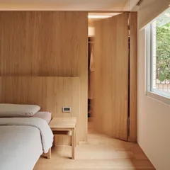 This image shows a minimalist bedroom where the wooden wall paneling seamlessly integrates a hidden door to the closet. This technique creates a clean, uncluttered look while maximizing space.