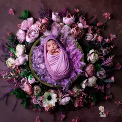 A peaceful newborn wrapped in purple, resting in a basket adorned with a wreath of lavender and purple flowers. The deep, calming colors make for a truly artistic infant portrait.