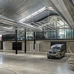 The main hall of the Automobile Design Studio is a vast, open space designed for showcasing and working on full-scale vehicle models. We retained the industrial feel with exposed ductwork and a high, skylit ceiling, while a sculptural concrete spiral staircase adds a touch of crafted elegance.