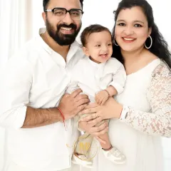 A classic family portrait where the parents and their baby boy are all smiling happily at the camera.
