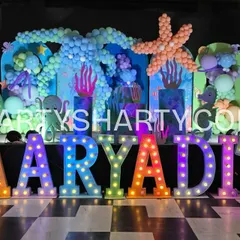 A vibrant underwater stage with a balloon-sculpted starfish and octopus, a mermaid tail prop, and rainbow-colored marquee letters.