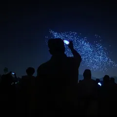 Silhouetted against the night sky, a crowd captures our drone formations on their phones. This image perfectly illustrates the shared experience and viral nature of our shows.