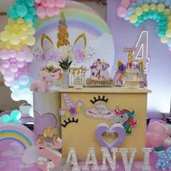 A unicorn-themed dessert bar setup with a large backdrop, rainbow balloon arch, and themed props.