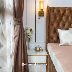 It's all in the details. This close-up shows the elegant bedside setup, with a sleek white and gold nightstand, a stylish wall sconce for reading, and the rich, diamond-tufted pattern of the headboard.