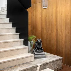 A sculpture of Nandi is placed at the base of the staircase, anchoring the space and reinforcing the home's curated, minimal aesthetic. The contrast between the black sculpture and the warm wood paneling is striking.
