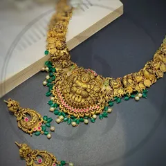 This handcrafted gold necklace features a central Lord Ganesha motif, a symbol of new beginnings. Intricate carvings and drops of green and pink stones make this a divine piece, perfect for invoking blessings on a special day.