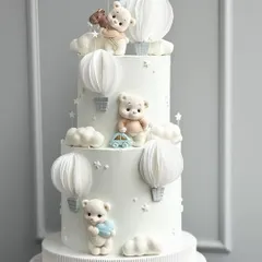 A stunning three-tiered all-white cake featuring adorable teddy bears, clouds, and paper hot air balloons.