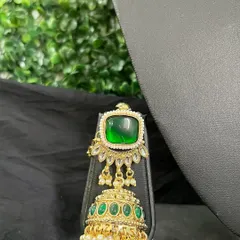 A unique earring with a large square green stone and a jhumka drop with smaller green stones.