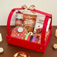 A beautiful red acrylic basket hamper for Diwali, filled with healthy snacks like millet namkeen, almond coffee bars, and a decorative diya.
