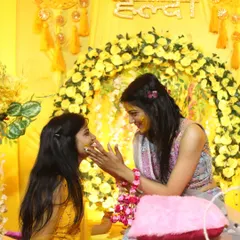 Sisters sharing a playful moment, smearing haldi on each other against the festive decor. Capturing these candid family moments is a core part of our wedding photography service.