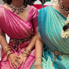 A close-up view of the coordinated drapes for the two sisters. You can see the neat, fan-like pleats on the pallu and how the sarees are accessorized with traditional waist belts (oddiyanam).