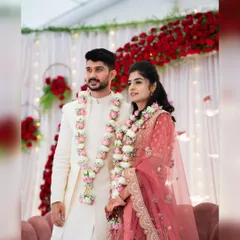 A lovely couple posing against the engagement stage we designed. The backdrop features a wall of red roses, white curtains, and delicate fairy lights, creating a warm and romantic ambiance for their ring ceremony.