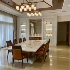A view of a grand dining space in the Tirupur residence, with a massive marble-top table and contemporary lighting, designed for hosting large family dinners.