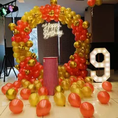 A simple and elegant circular balloon arch in red and gold. This setup includes a 'Happy Birthday' neon sign and a large light-up number '9', with loose balloons on the floor for a playful touch.
