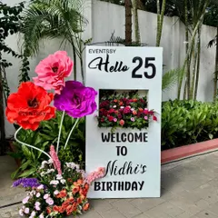 The 'Hello 25' welcome sign for the milestone birthday, decorated with both fresh flowers and large, colorful paper flowers.