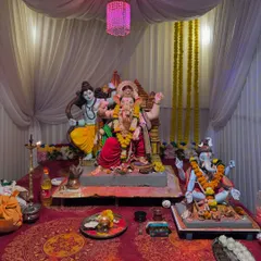 A full view of the pandal setup for the 'Gokul Nagari Cha Maharaja' 2024 event. This shows the simple yet clean arrangement with white fabric draping, a pink chandelier, and a well-lit space for multiple idols.