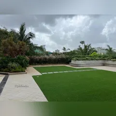 This wide shot showcases the expansive lawn area, designed for corporate events and employee recreation. The space is framed by raised planters filled with ornamental grasses and trees, providing a natural boundary and visual interest.
