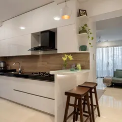 A look at a modern kitchen renovation we completed, designed for seamless cooking and entertaining. This space features handleless glossy white cabinets for a clean, minimalist look, a functional breakfast counter for casual meals, and a warm wood-textured backsplash. We focus on smart layouts that combine high-end appliances with ample storage and workspace.