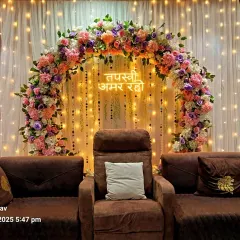 An elegant backdrop for a Jain Tapasvi ceremony. I used a beautiful arch of pastel flowers, a custom neon sign with the blessing "Tapasvi Amar Raho," and warm lighting to create a serene and respectful setting in the family's home.