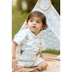 A classic portrait of a little boy during his pre-birthday twin photoshoot. Dressed in a smart shirt and suspenders, he sits in front of a lace teepee, looking thoughtfully into the distance.