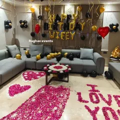 A closer look at the romantic living room setup. The decoration features a rose petal pathway, hearts on the floor, and a 'Happy Birthday Wifey' balloon arrangement with black and gold balloons.