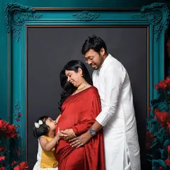 A heartwarming family maternity photo where the older sibling kisses the baby bump. This shot, framed by a dramatic floral and frame setup, beautifully captures the family's excitement and the special connection between siblings before the new baby even arrives.