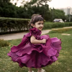 A little girl in a beautiful purple dress twirls happily on the grass. Outdoor shoots are perfect for capturing these moments of pure, uninhibited joy.