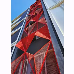 An upward-looking view of the red facade, highlighting the dynamic, three-dimensional quality of the triangular panels against the blue sky.