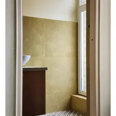 A view into a compact powder room, where patterned floor tiles create a strong graphic statement. The warm, metallic wall tiles and dark wood vanity add a sense of richness and depth to the small space.