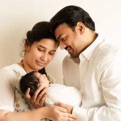 New parents gaze lovingly at their swaddled newborn, their heads touching in a moment of quiet adoration, captured in a bright and airy studio setting.